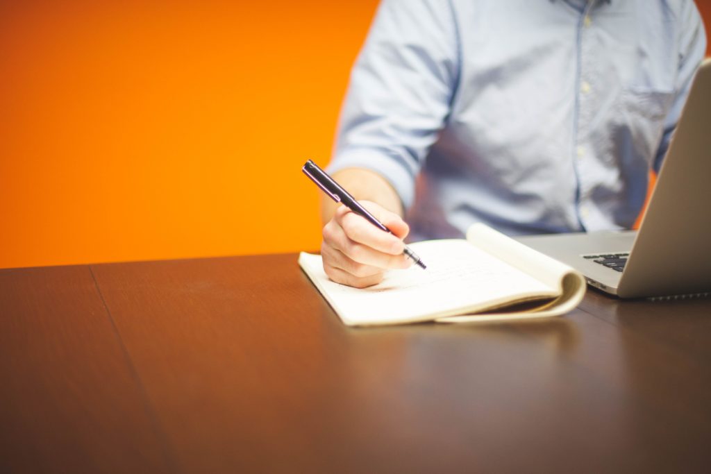 Man sitting at desk with orange wall behind him Photo by Startup Stock Photos from Pexels