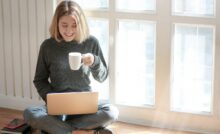 Woman sitting on the floor sipping on her drink and working on her laptop